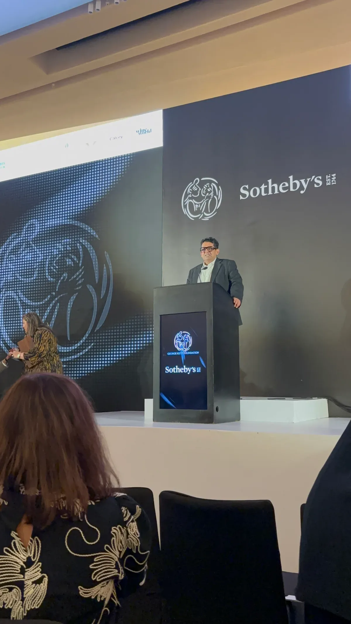 Malaka Talwatte speaking at the podium under the Sotheby's and George Keyt Foundation backdrop.