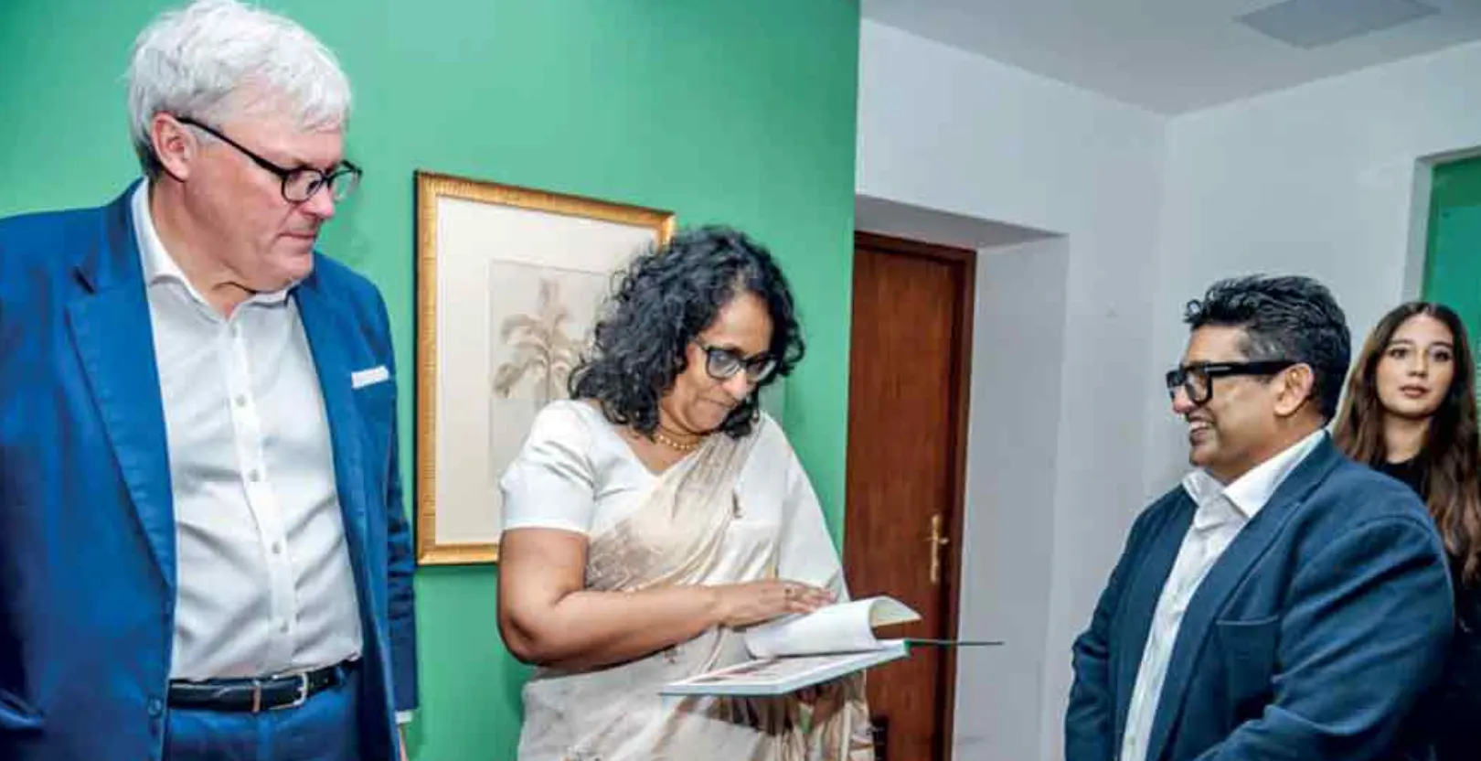 Malaka Talwatte with guests examining the exhibition book beside a framed nineteenth-century drawing.