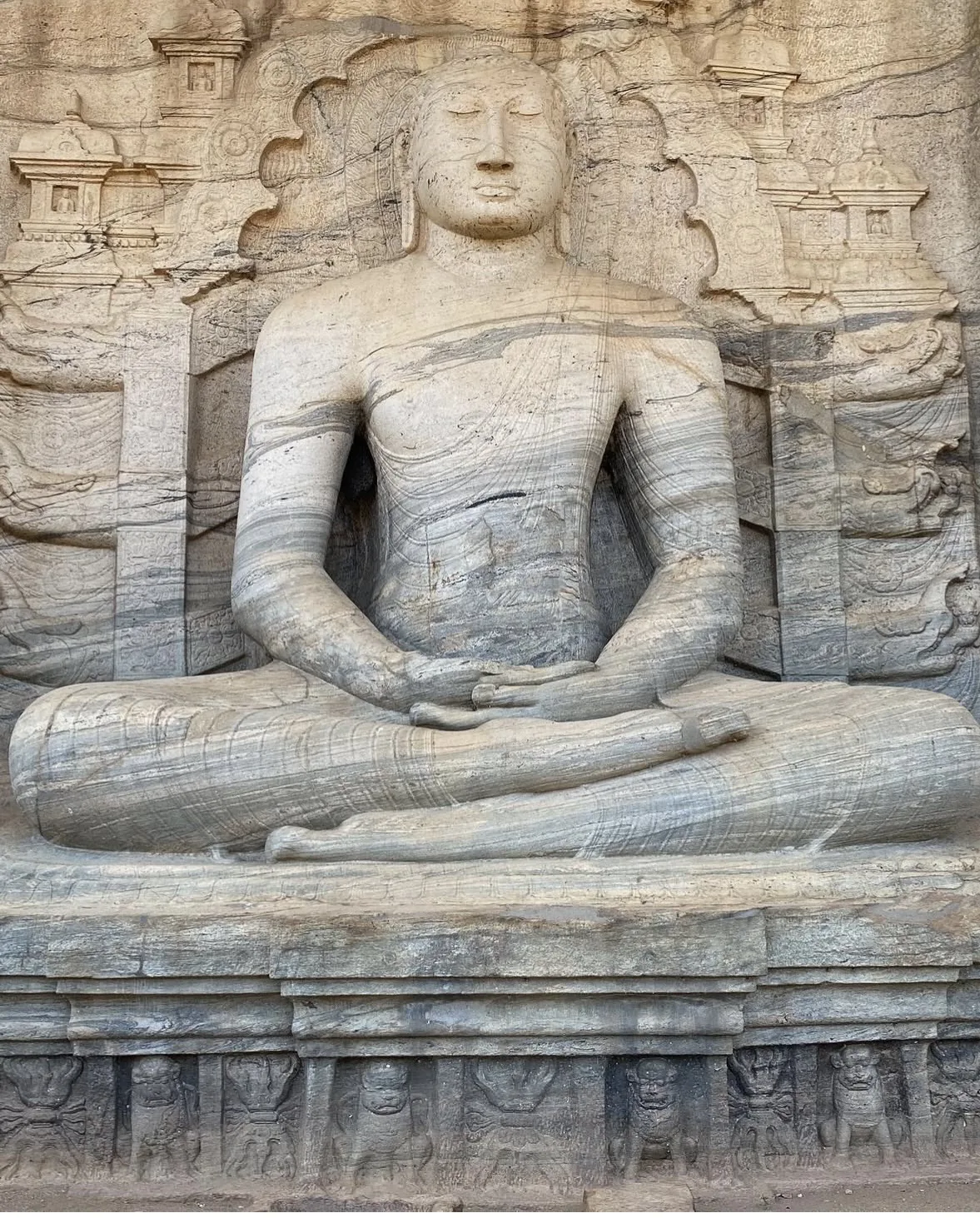 The seated Buddha in meditation at Gal Vihara, in the dhyana mudra on a lotus throne, a carved screen of makara and small seated Buddhas behind the shoulders.