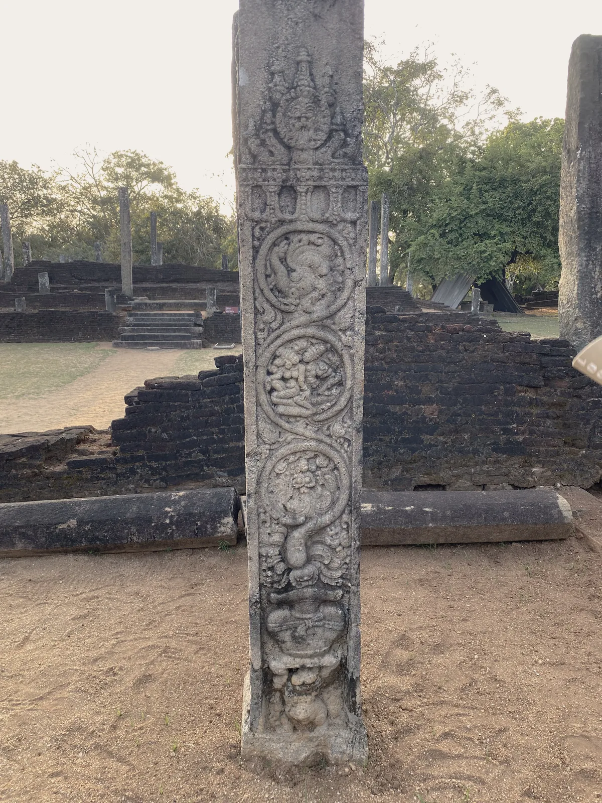 A pillared stone relic-house in the Sacred Quadrangle at Polonnaruwa, its rows of stone pillars standing, a Buddha image visible at the far end, its upper timber storey lost.