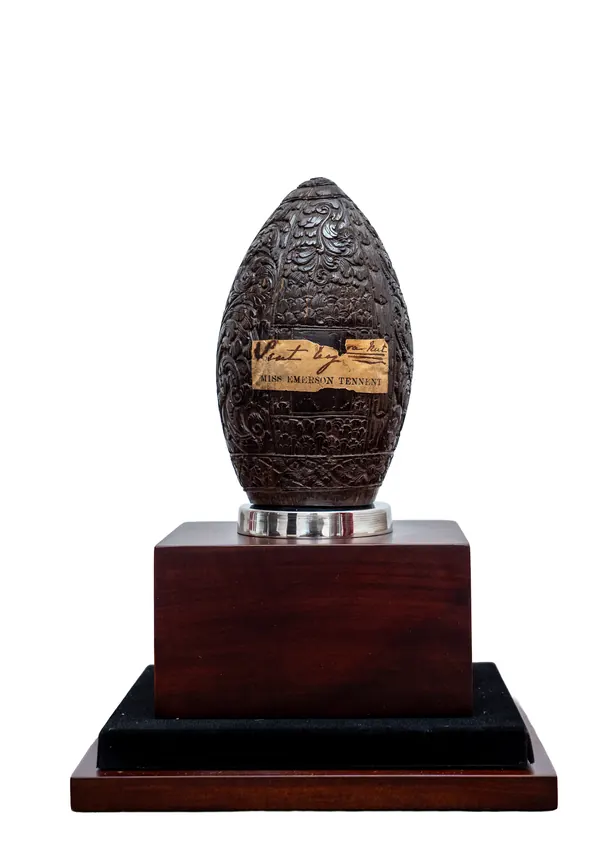 A carved coconut shell on a turned wooden stand, its surface worked in dense foliate relief.