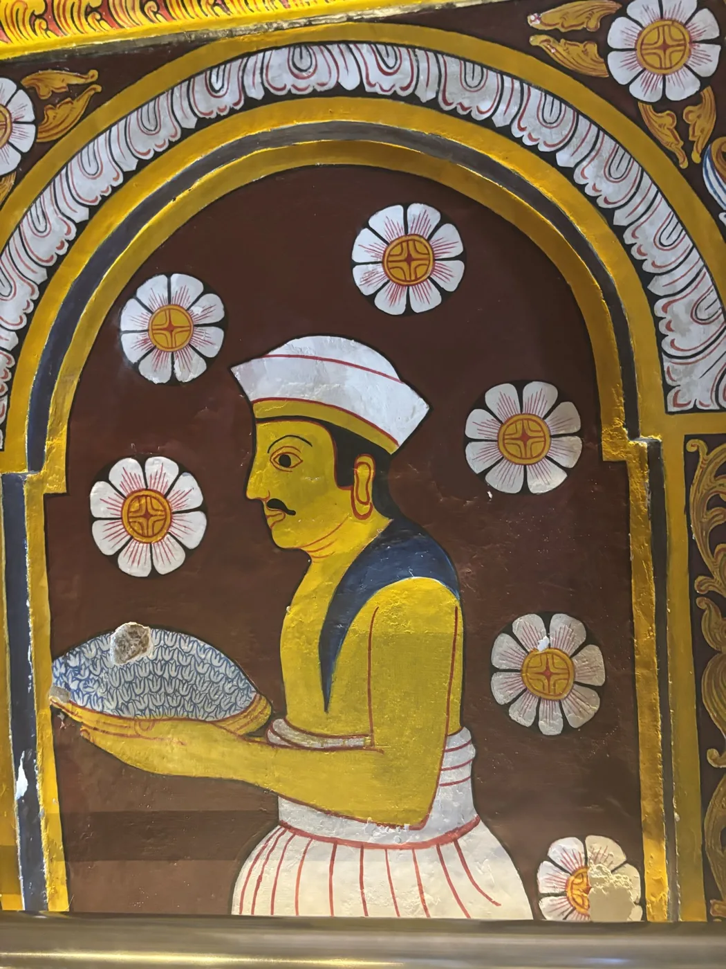 A painted figure holding a tray of flowers, set among lotus rosettes within a gilded arch.