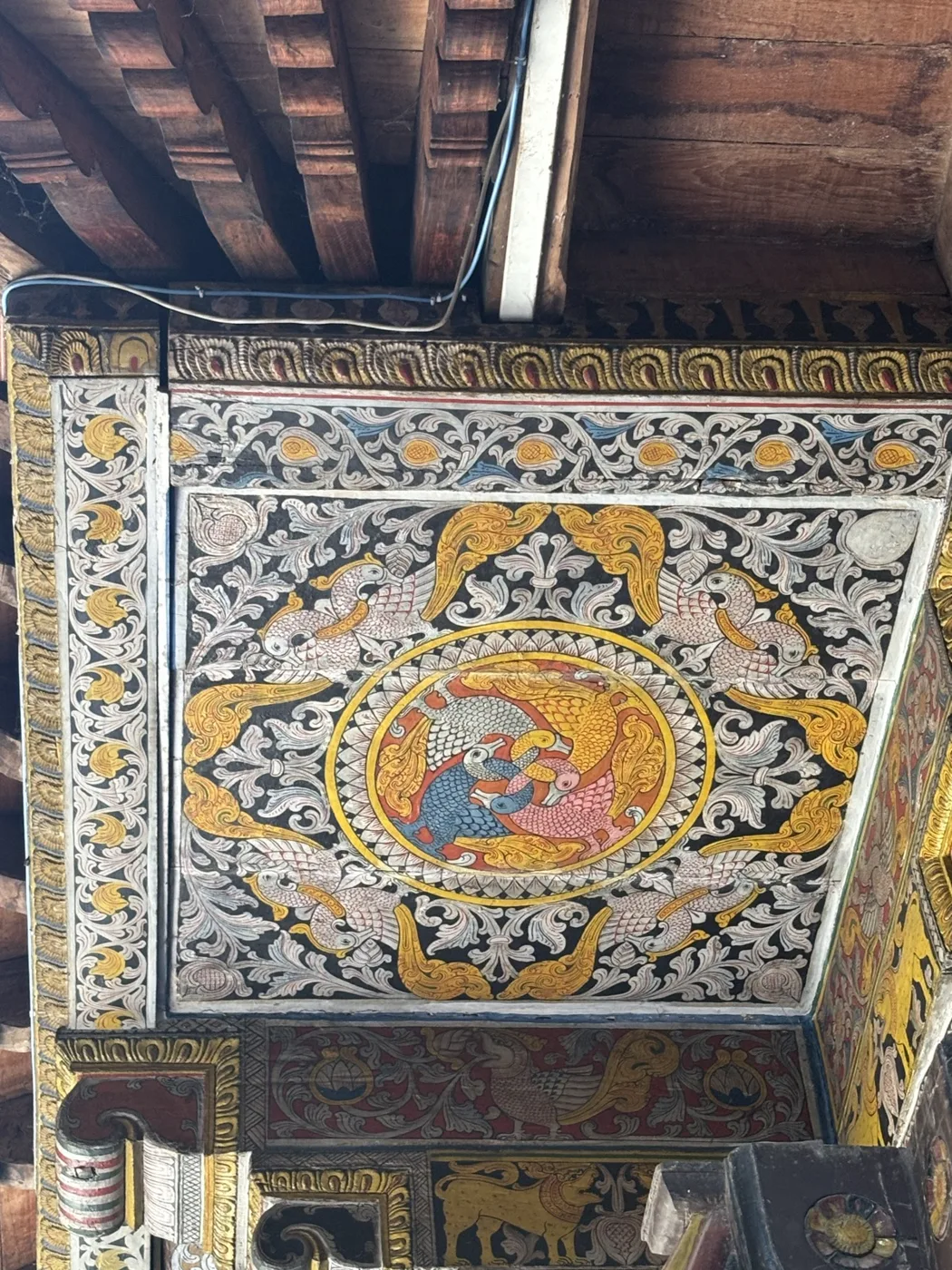 A painted ceiling corner with a central figural medallion ringed by dense gold scrollwork and swan motifs.