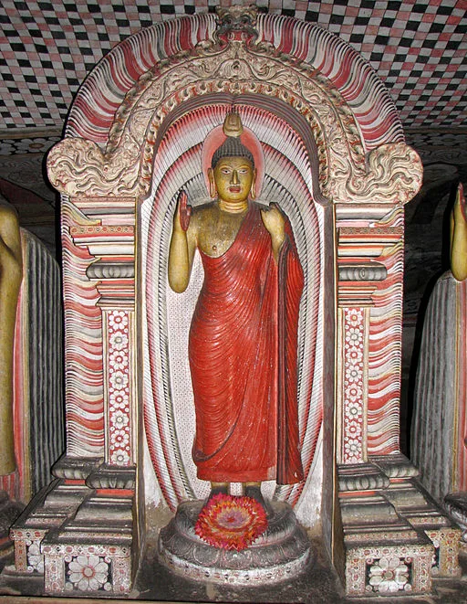 A makara torana arch framing a standing Buddha, composite makara creatures rising to a demon mask at the crown.